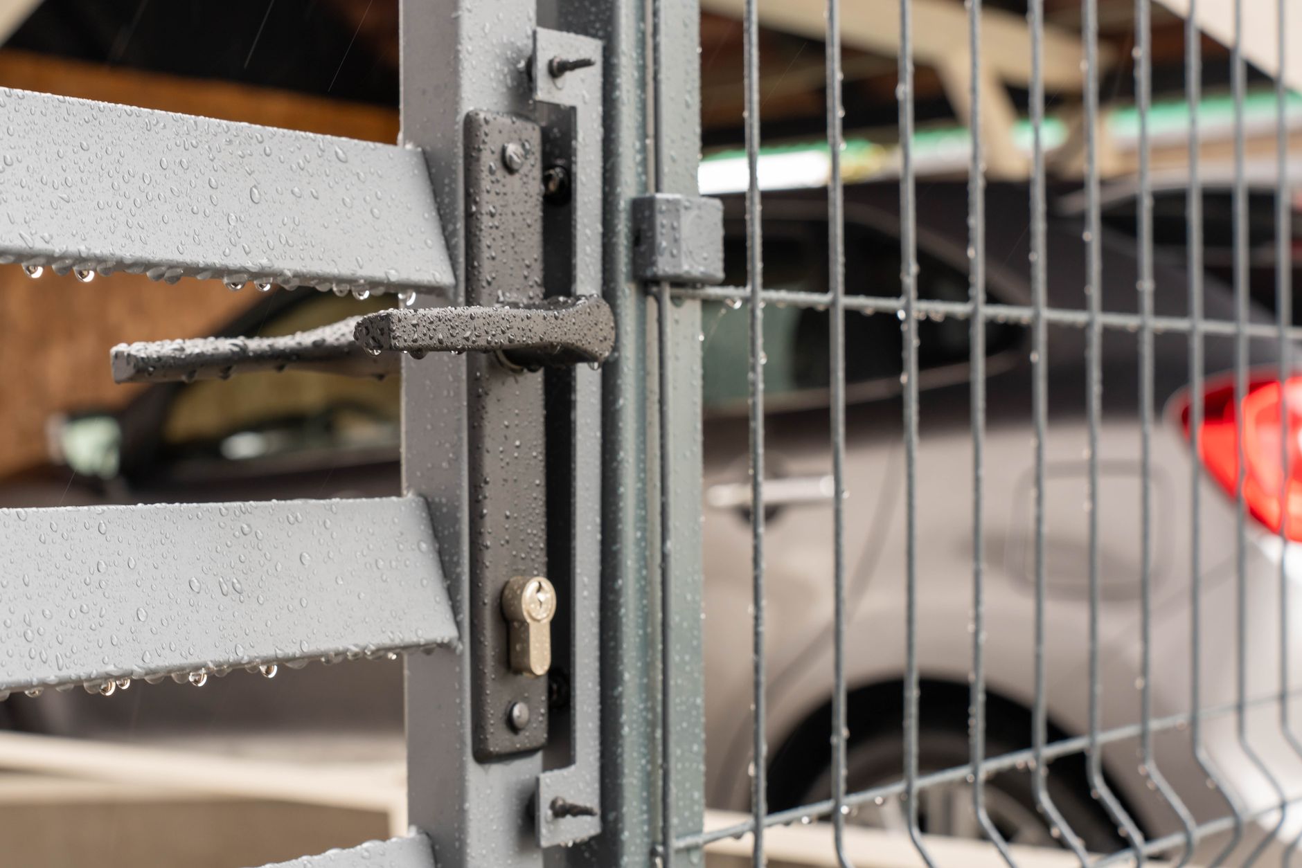 Detailed view of a wet metal gate with raindrops and a parked car in the background in Mount Pleasant, SC